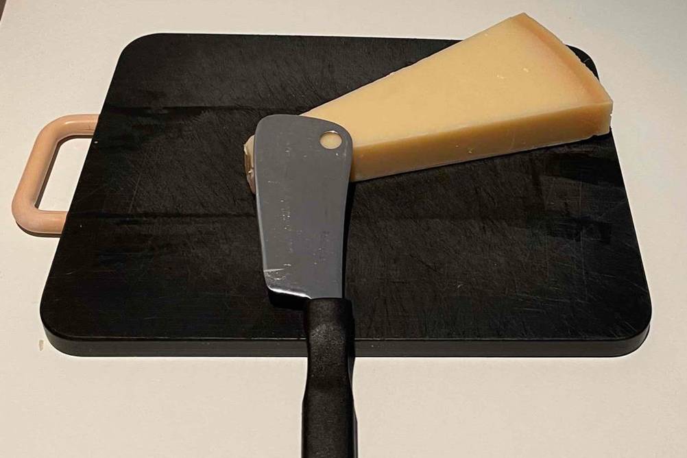 Käsemesser getestet: Ein Messer und ein Käse liegen auf einem schwarzen Schneidebrett