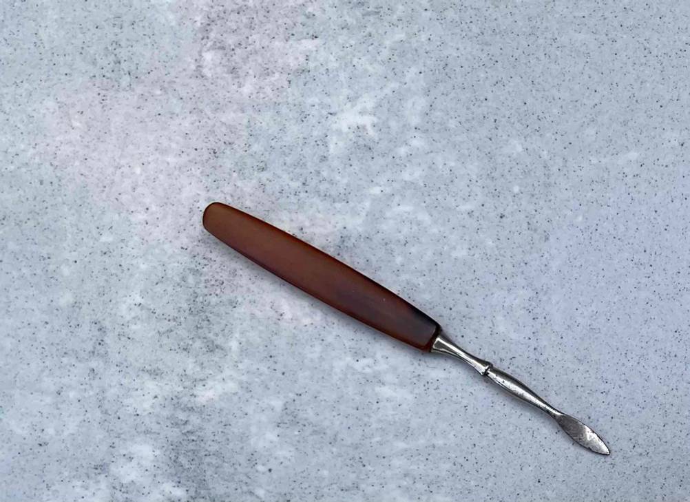 Nagelhautschieber im Test: Nagelhautschieber liegend auf einer grauen Fläche mit braunem Griff.
