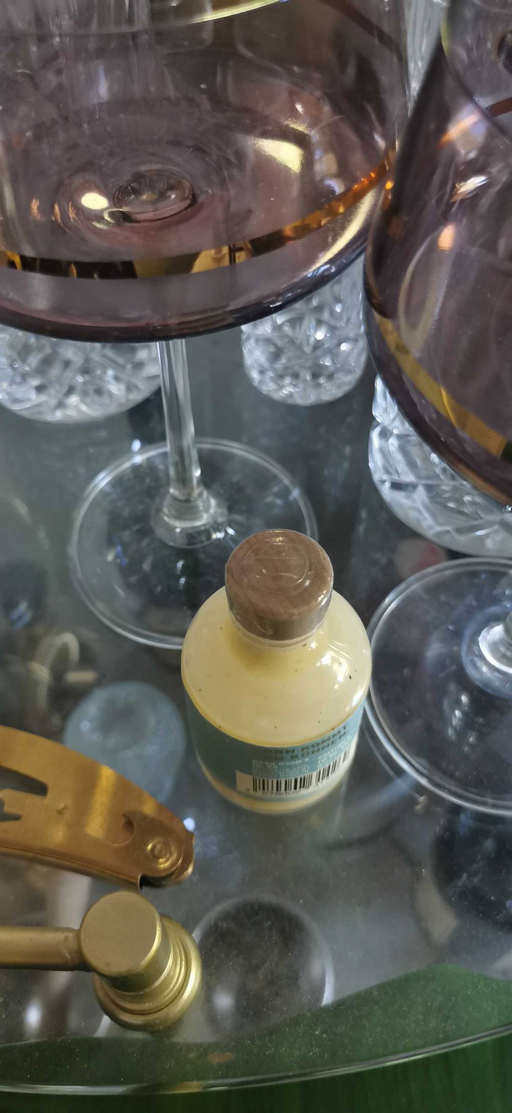 Eine getestete Flasche Eierlikör von oben auf einem Glastisch neben wei Weingläsern.