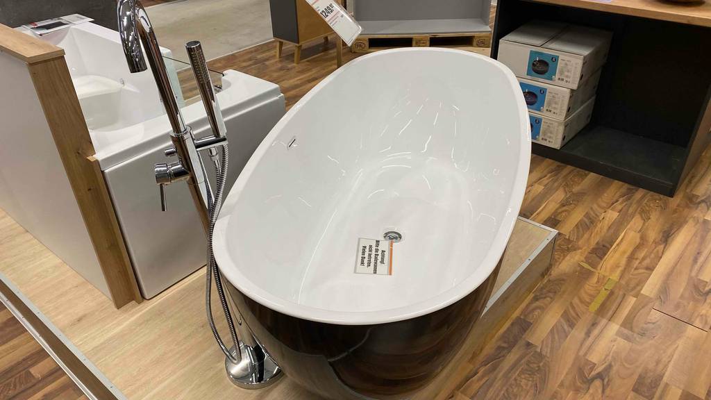 Eine freistehende Badewanne auf einem Sockel neben einer freistehenden Armatur.