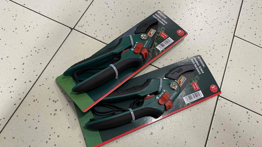 Im Test: Zwei verpackte Amboss-Gartenscheren liegen leicht übereinander auf einem Fließenboden