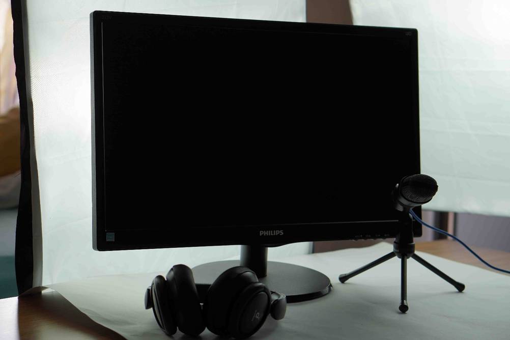 Auf einer hellen Oberfläche steht ein getesteter Monitor und davor Kopfhörer und ein Mikrofon