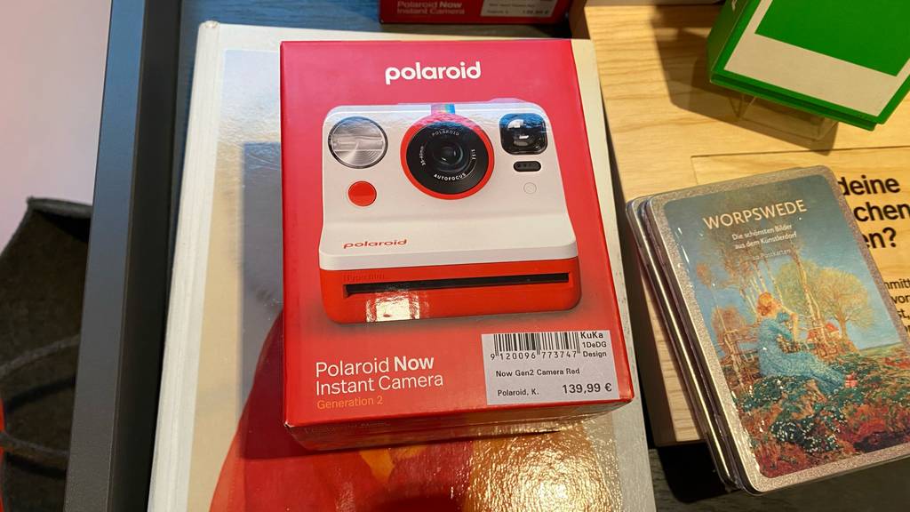 Eine getestete, originalverpackte Polaroid-Kamera liegt auf einem Stapel anderer Produkte.