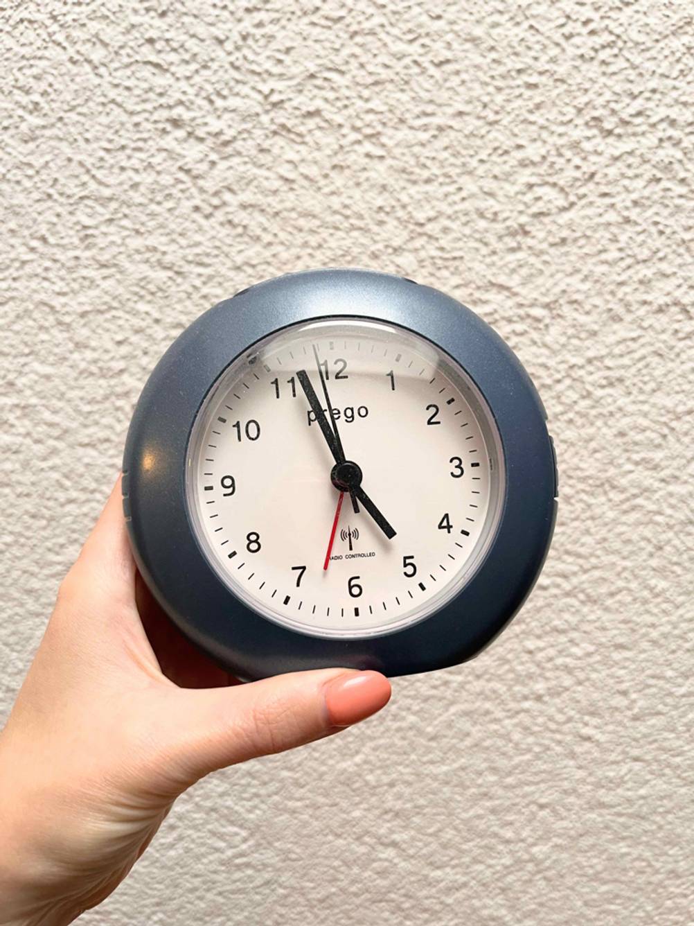 Eine Hand hält einen getesteten Funkwecker (analog) vor eine helle Wand.