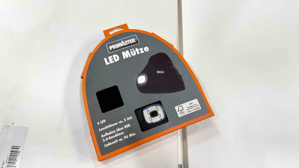 Im Test: Die LED-Mütze in Schwarz liegt innerhalb eines grau-orangefarbenen Verpackungskartons auf einer weißen Oberfläche.