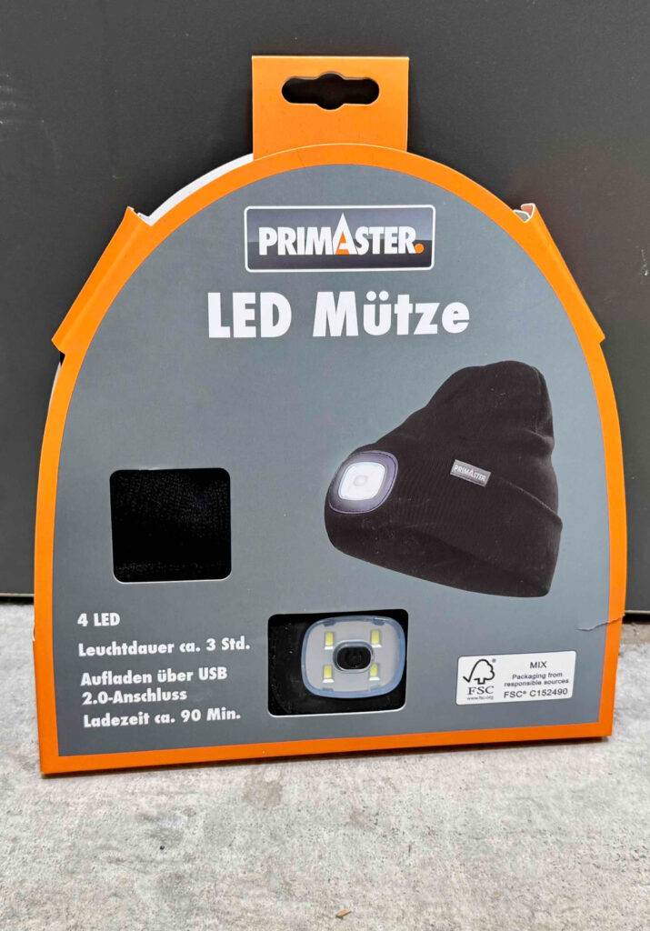 LED-Mützen-Test: Ein schwarzes Modell befindet sich ein einem grau-orangefarbenen Verpackungskarton mit Sichtfenster auf die integrierte LED-Lampe.