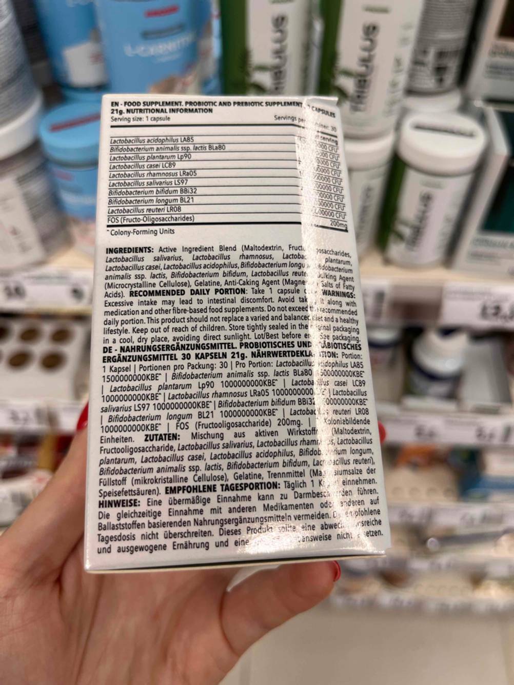 Probiotika im Test: Eine Hand hält die Rückseite mit dem Inhalstoffen vor ein Regal