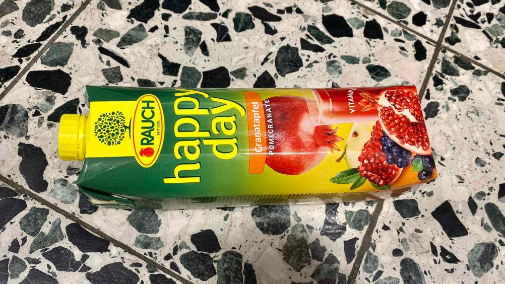 Eine Packung des geteteten Granatapfelsaftes liegt horizontal auf einer Steinfläche.