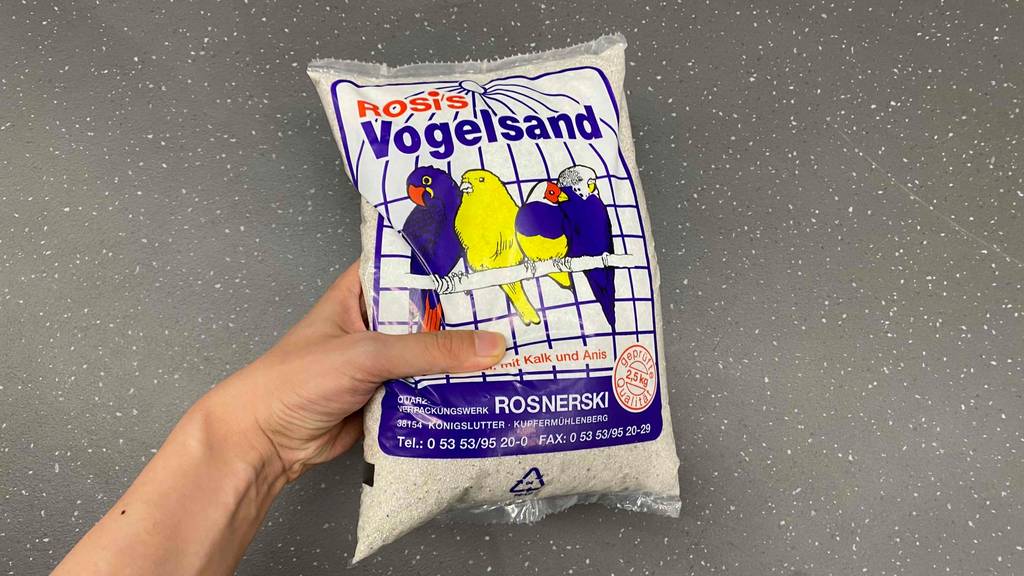 Vogelsand im Test: eine Packung Vogelsand der Marke Rosis wird in der Hand gehalten.