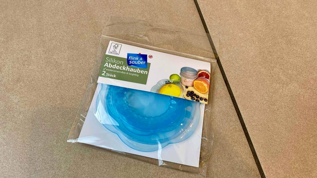 Silikondeckel getestet: ein blauer Silikondeckel, welcher sich in der Verpackungn befindet, liegt auf einem Boden.