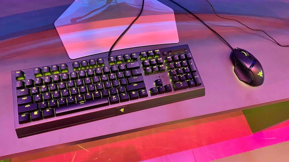 Auf einem Tisch vor einem Monitor befindet sich eine getestete Gaming-Tastatur und -Maus.