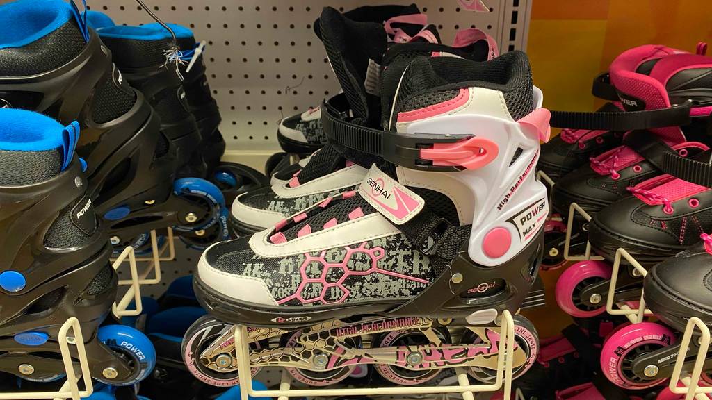 In einem Regal neben anderen Produkten steht ein Paar getestete Inline-Skates für Kinder.