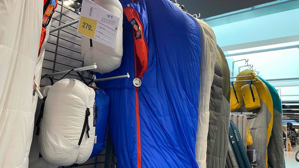 Daunenschlafsack-Test: Aufbewahrungstaschen von Daunenschlafsäcken und daneben verschiedene Daunenschlafsäcke in einem Regal hängend.