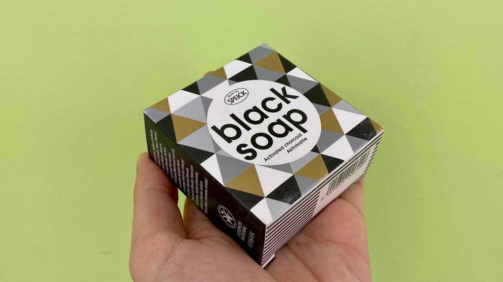 Schwarze Seife getestet: Eine Hand hält eine Packung Seife vor eine grünen Hintergrund