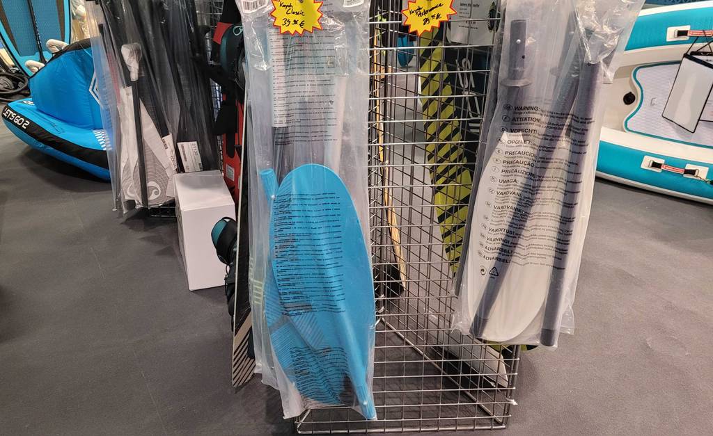 Kajak-Paddel im Test: blaues Kajak-Paddel in einer Plastikverpackung in einem Geschäft neben weißem Kajak-Paddel hängend.