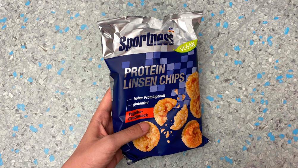 Protein-Chips im Test: Eine Packung wird von einer Hand vor einen Fließenboden gehalten