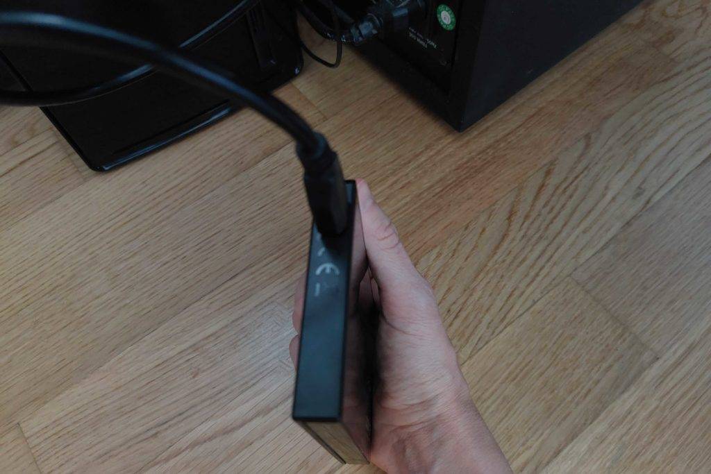 SSD Festplatte im Test: Eine Hand hält eine angesteckte Festplatte hoch im Hintergrund ein Computer