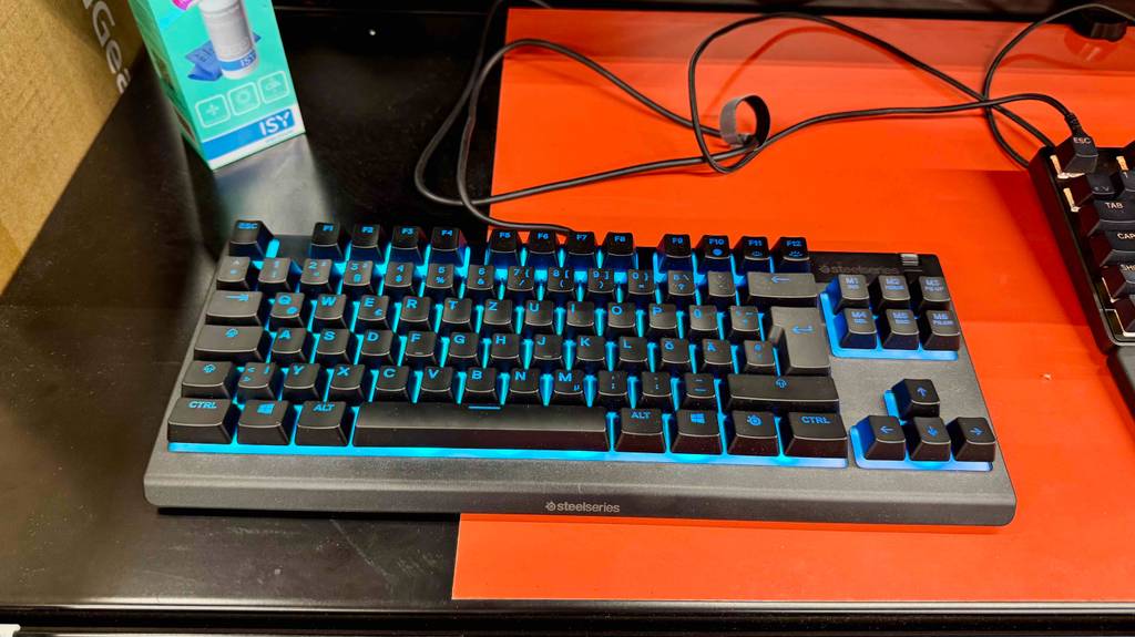 Die SteelSeries-Tastatur im Test steht mit beleuchteter Tastatur auf einem orangefarbenen Tisch.
