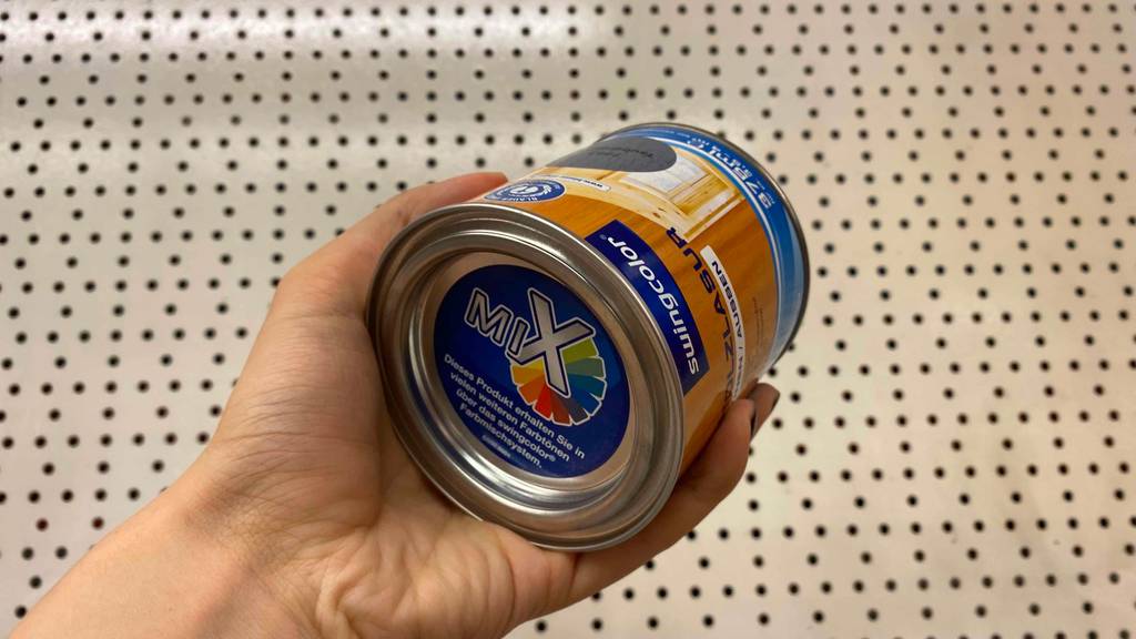 Holzlasur getestet: Eine Hand hält eine Dose Lasur vor einen hellen Untergrund