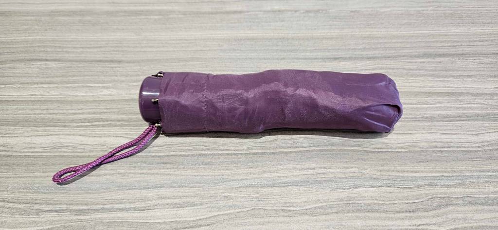 Ein getesteter Taschenschirm zusammengefaltet in seiner Schutzhülle auf einem grauen Boden.