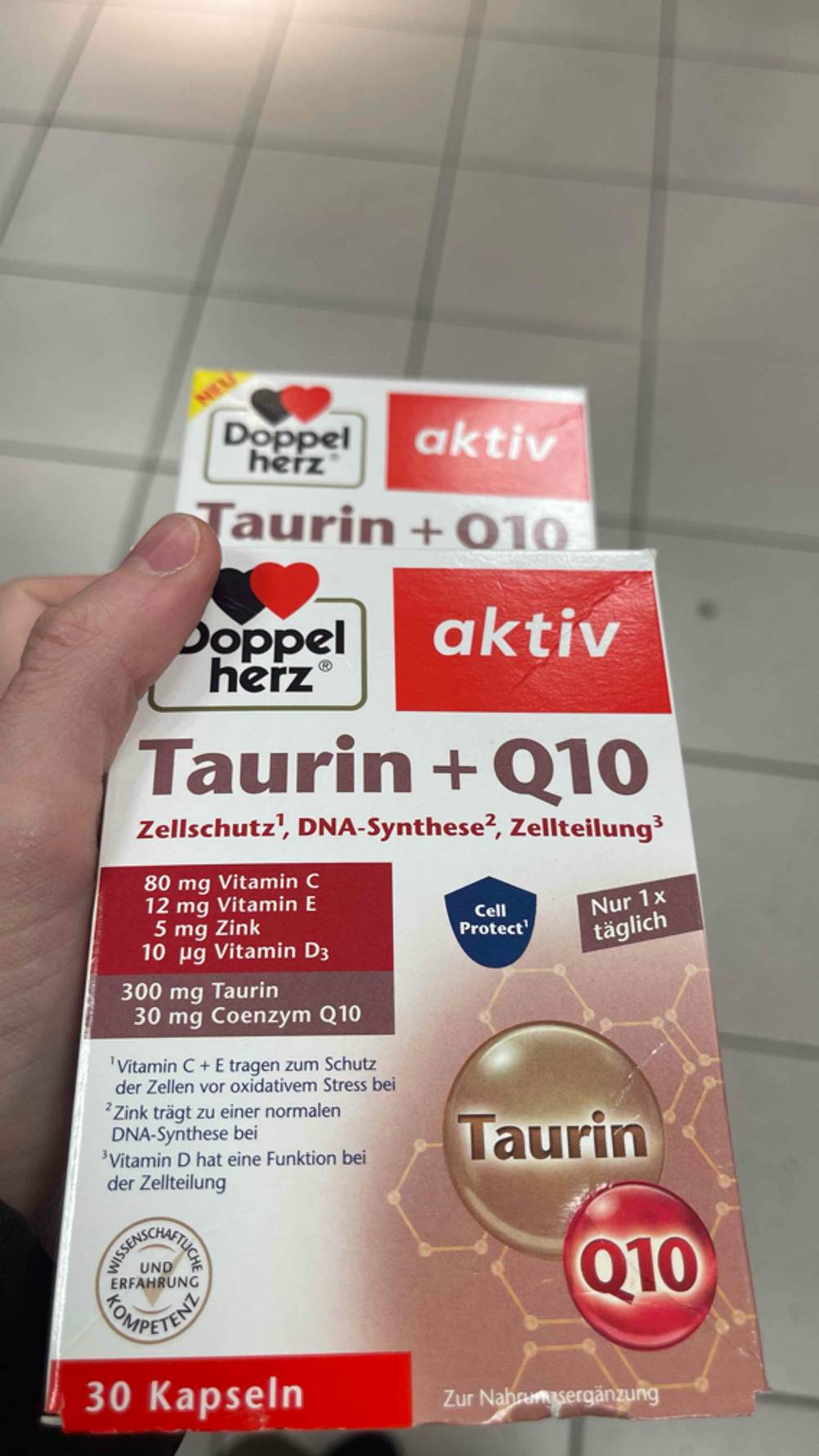 Zwei Packungen mit getesteten Taurin-Kapseln darin, werden in der Hand gehalten.