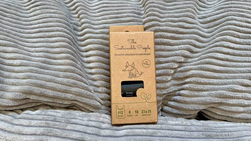 Getestete biologisch abbaubare Hundekotbeutel, die sich in der Verpackung befinden und vor einem Kissen platziert sind.