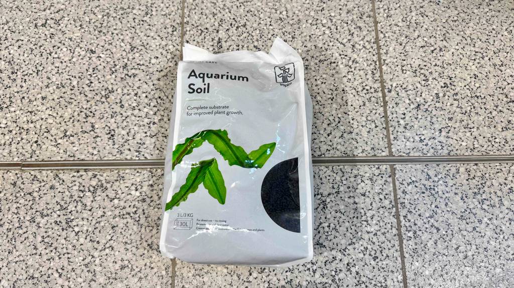 Aquarium Bodengrund im Test: Die weiße Kunststofftüte für 130 Liter liegt auf einem Fliesenbelag.