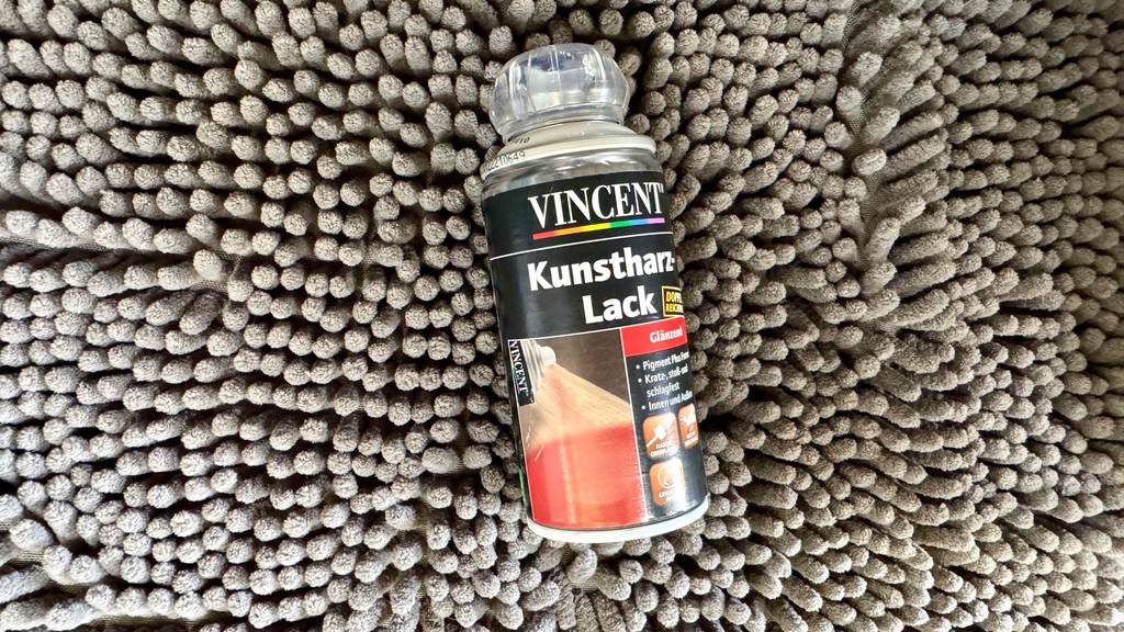 Eine Dose getesteter Kunstharzlack liegt auf einer grauen Noppenfläche.