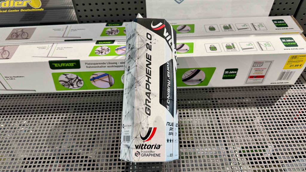 Eine Verpackung mit dem getesteten Rennrad-Reifen (23-622) liegt auf Fahrrad-Rahmenhalter im Geschäft.