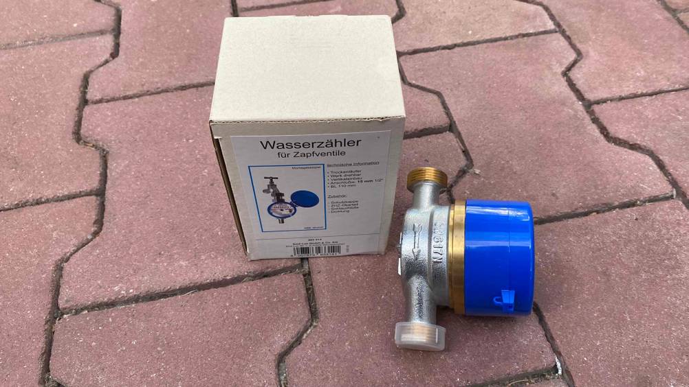 Wasserzähler getestet: Ein Wassserzähler neben seiner Originalverpackung auf einem Steinboden