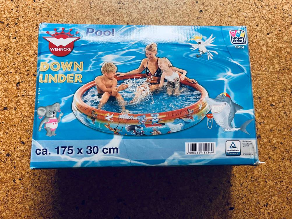 Ein getesteter aufblasbarer Pool in seiner Verpackung auf einem Holzboden liegend.