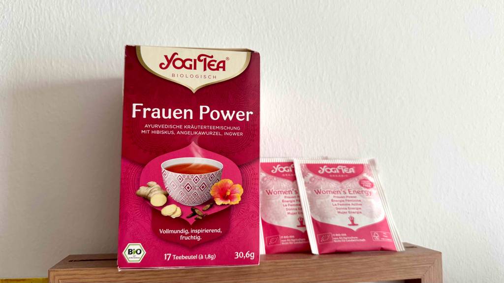 Zwei Teebeutel des getesteten Yogi Tees Frauen Power stehen neben der roten 17-Stück-Verpackung vor einer weißen Wand.