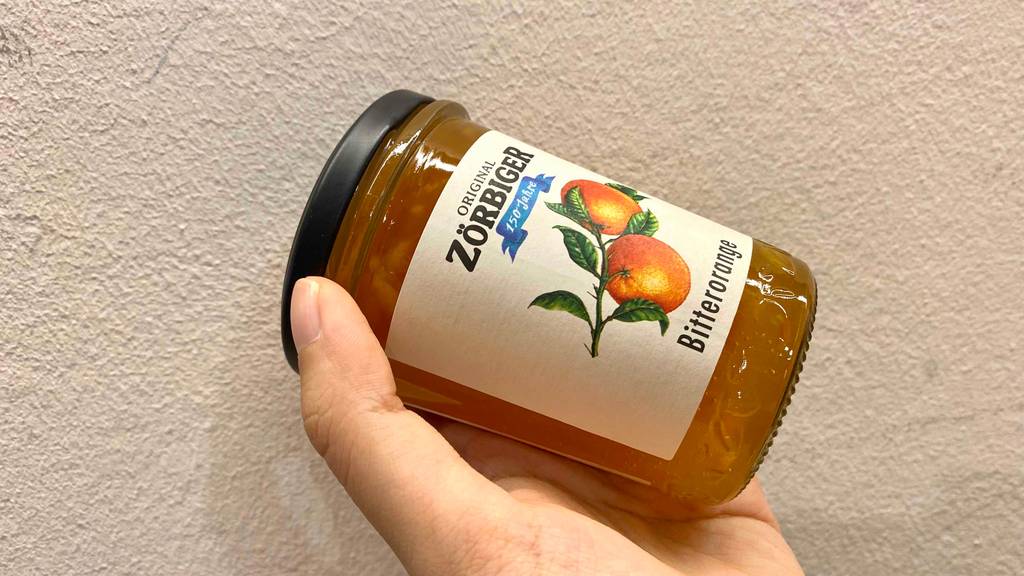 Getestete Orangenmarmelade mit Hand vor einer Wand gehalten
