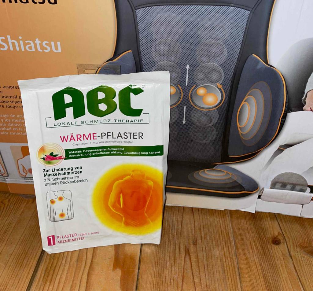 Wärmepflaster getestet: ein eingepacktes Wärmepflaster dere Marke ABC steht vor der Verpackung eines Massagestuhls.