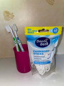 Zahnseide Packung und zwei Zahnbürsten in Zahnputzbecher.