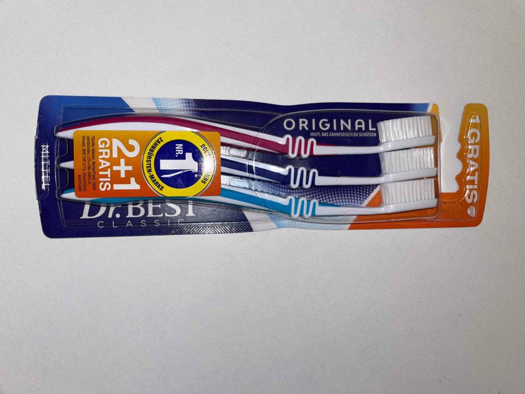Zahnbürste im Test: drei Zahnbürsten in verschiedenen Farben befinden sich in der Verpackung, welche auf einer weißen Fläche.