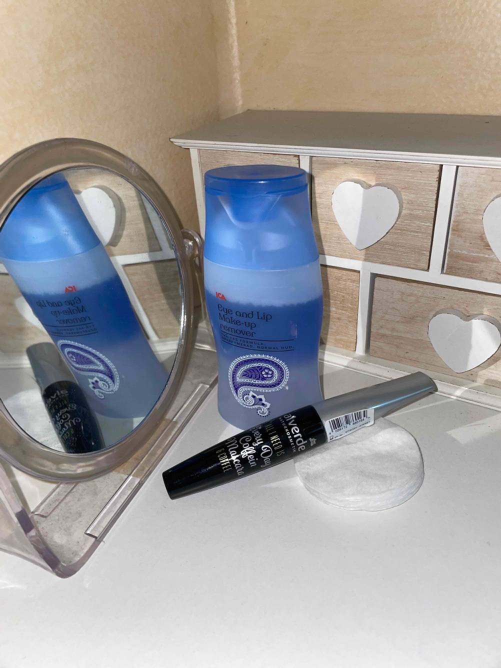 Augen-Make-up-Entferner, Wimperntusche, Wattepad und Kosmetikspiegel zu sehen.