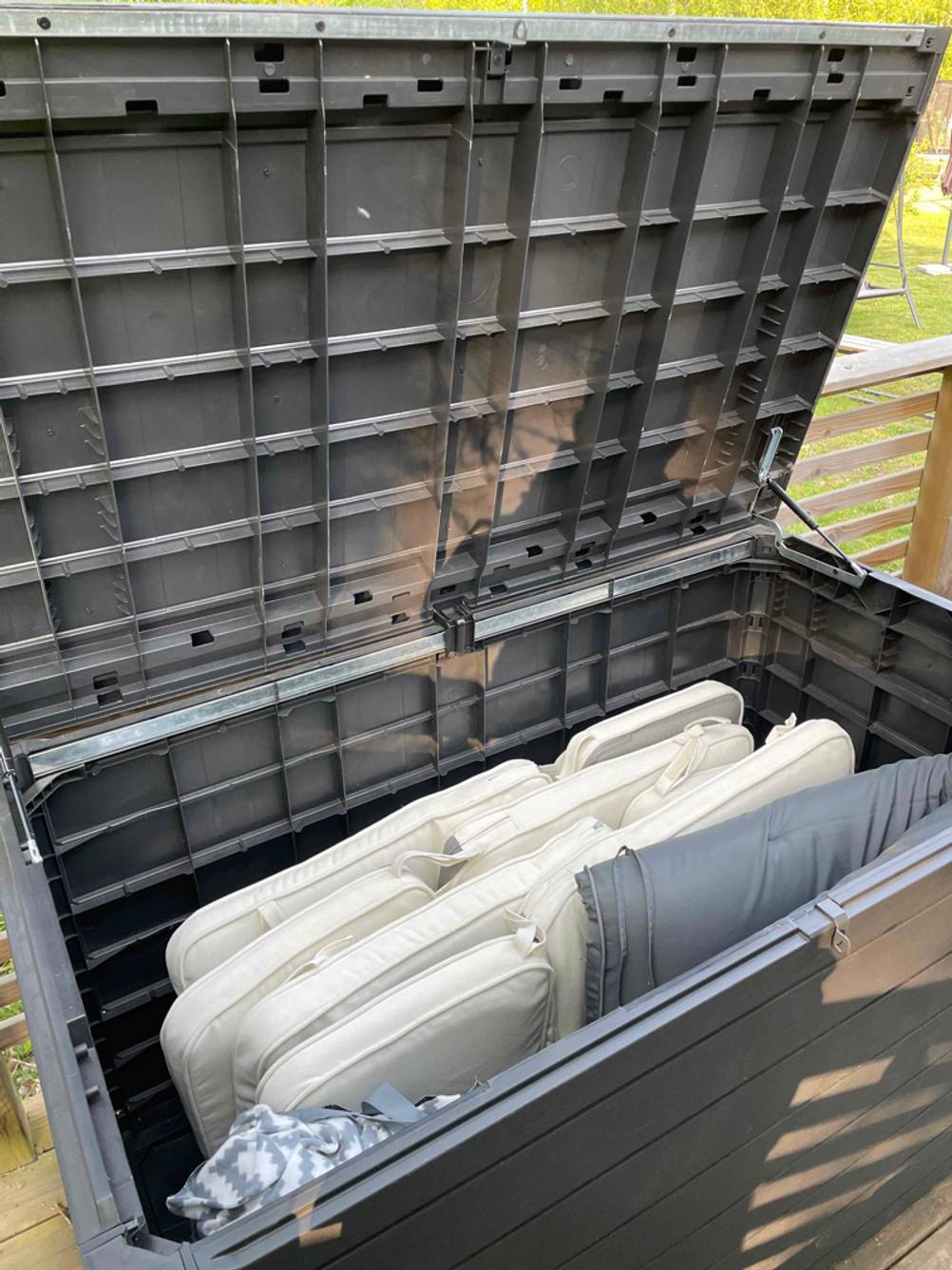 Eine geöffnete Auflagenbox mit Sitzauflagen darin schräg von vorne. Die Auflagen sind beige.