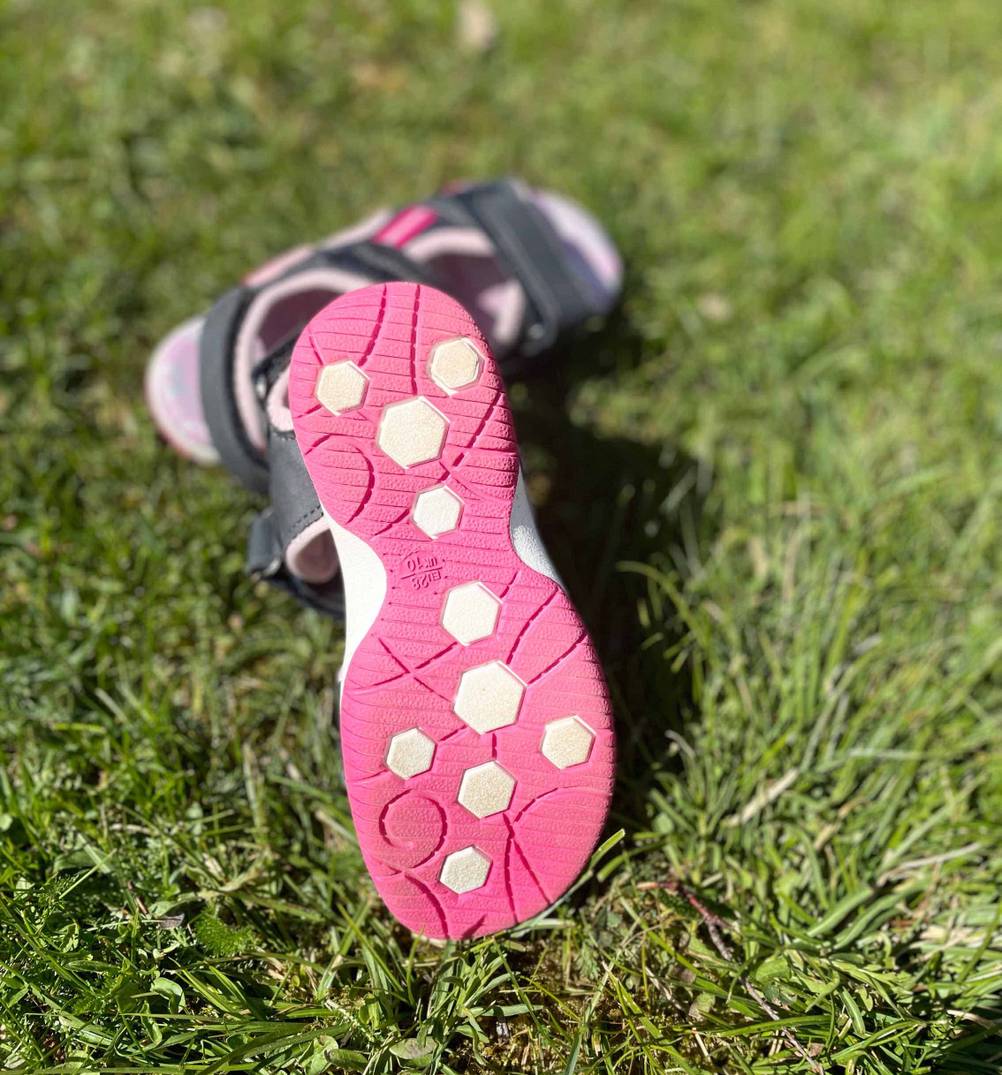 Kindersandalen-Test: pinkfarbene Sohle von Kindersandale ersichtlich, die auf einer Wiese platziert ist.