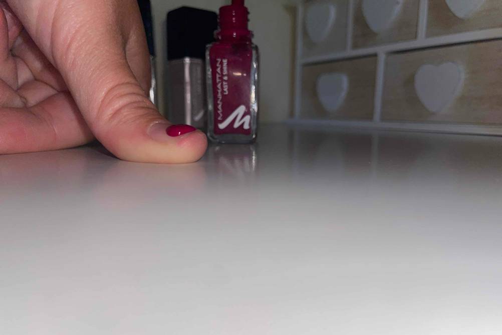 Roter Nagellack auf einem Fingernagel Nagellack in Flasche zu sehen.
