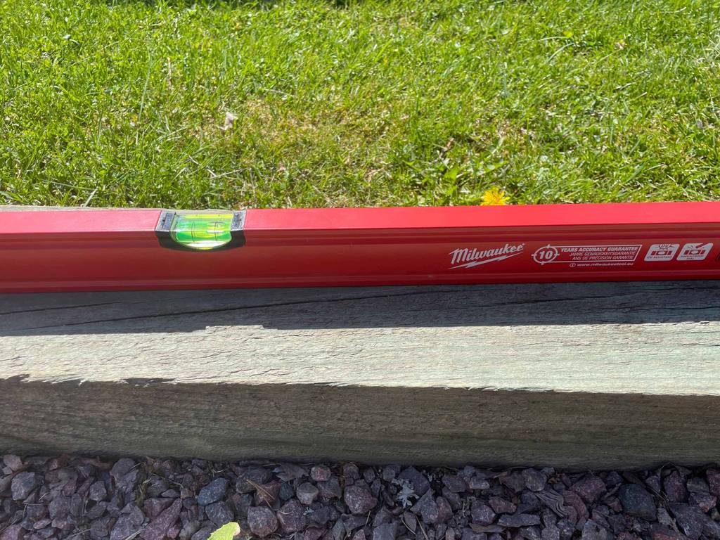 Wasserwaage im Test: eine rote Wasserwaage ist in einem Garten auf ein Holzstück gelegt.