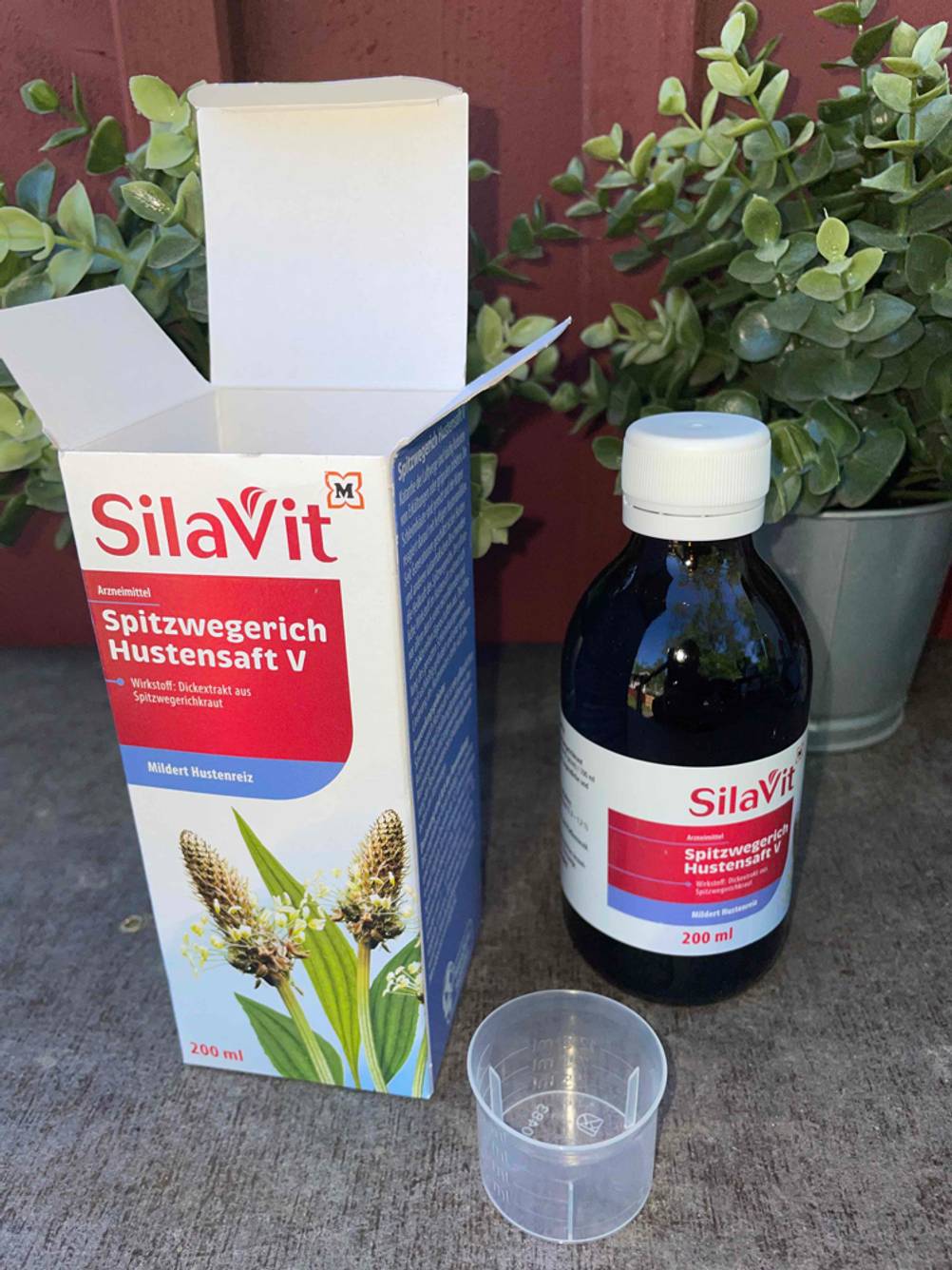 Hustensaft, Kappe zum Dosieren und Verpackung zu sehen.