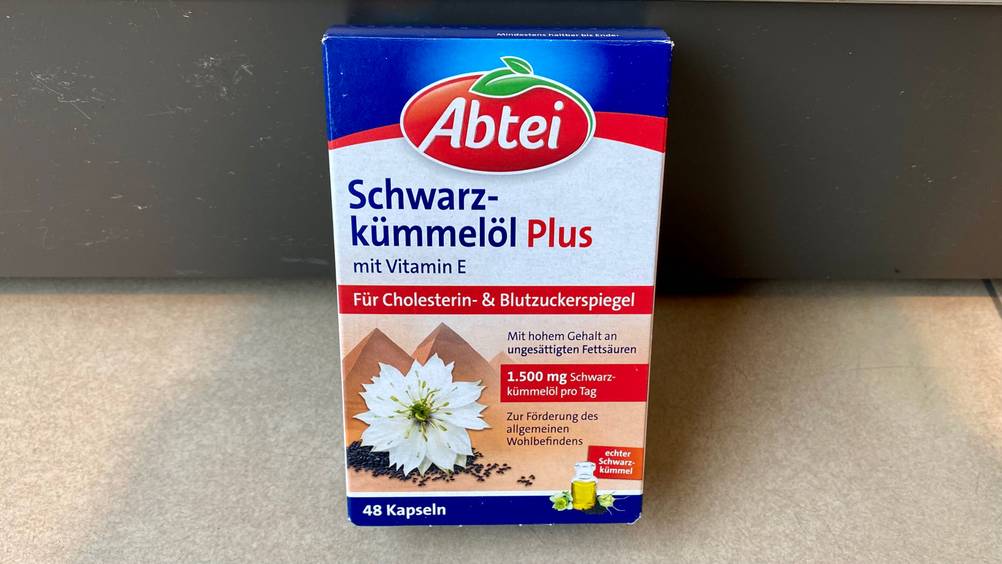 Eine Packung getestete Schwarzkümmelöl-Kapseln vor einer dunklen Wand.