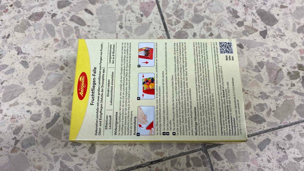 Eine Packung der getesteten Fruchtfliegenfalle liegt mit ihrer Rückseite nach oben auf einem Steinboden