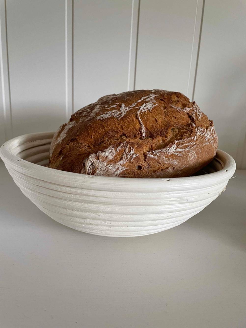 Vor einer hellen Wand steht ein getestetes Gärkörbchen mit einem Brot im Inneren.