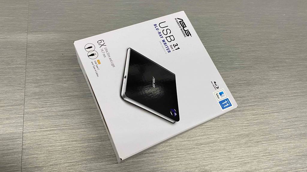 Im Test: Ein verpackter Blu-Ray Brenner von asus liegt auf einem grauen Boden.