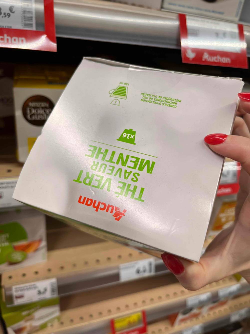 Grüner-Tee-Kapseln im Test: Eine Hand hält eine Packung Tee Kapseln hoch, im Hintergrund ein Regal