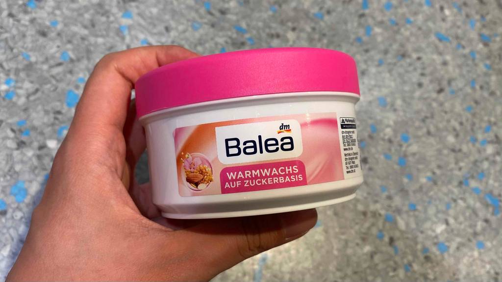 Warmwachs getestet: Eine Hand hält eine Dose Wachs vor Fließenboden
