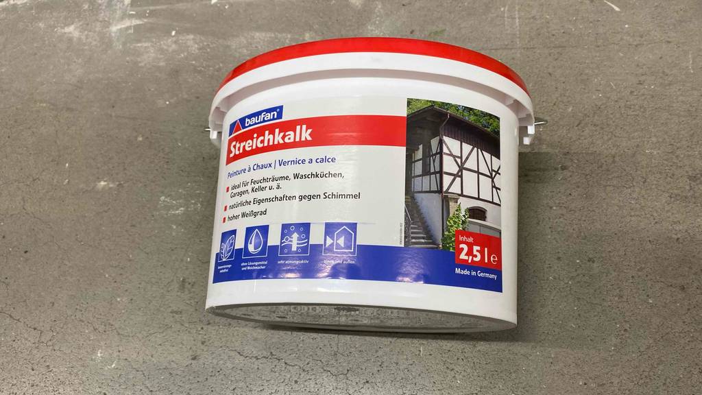 Ein Eimer getestete Kalkfarbe liegt auf einem Betonboden.