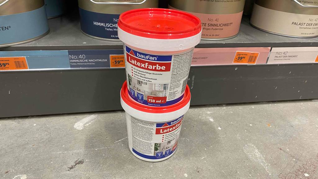 Zwei Eimer der getesteten Latexfarbe stehen übereinander vor einem Regal.